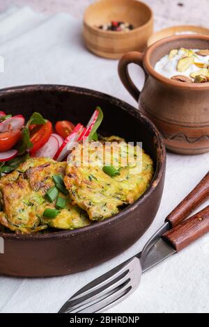 Frittelle di zucchine, piatto vegetariano con zucchine appena grattugiate, tuorlo d'uovo, pistacchi e cipolla in rustica ciotola di ceramica servita con insalata verde, Foto Stock