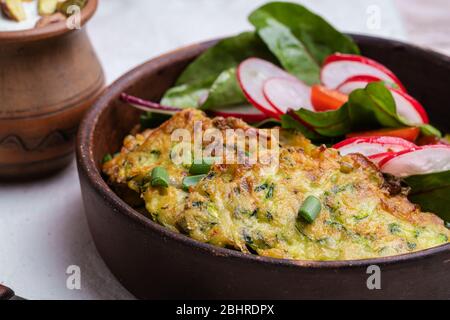 Frittelle di zucchine, piatto vegetariano con zucchine appena grattugiate, tuorlo d'uovo, pistacchi e cipolla in rustica ciotola di ceramica servita con insalata verde, Foto Stock