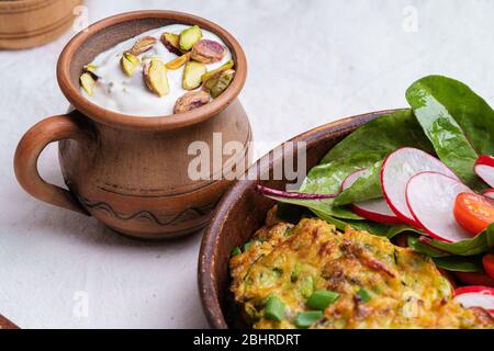 Frittelle di zucchine, piatto vegetariano con zucchine appena grattugiate, tuorlo d'uovo, pistacchi e cipolla in rustica ciotola di ceramica servita con insalata verde, Foto Stock