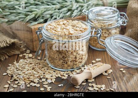 Vasi di fiocchi d'avena, orecchie d'avena verdi e sacco su tavola di legno. Foto Stock