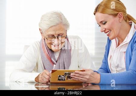 Donna anziana felice guarda un vecchio album fotografico con sua figlia Foto Stock