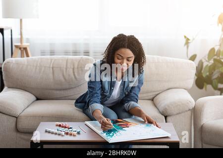 Giovane donna nera disegno immagine da numeri con su tela a casa Foto Stock