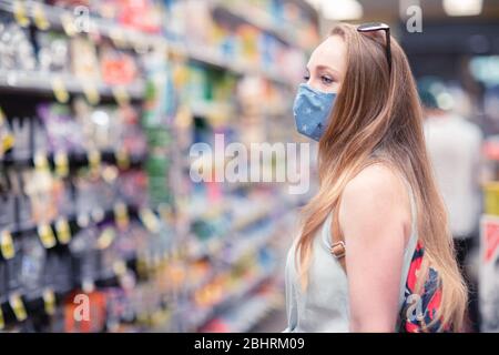 Una giovane donna in un grande negozio di alimentari con maschera facciale. Persone che indossano maschere di stoffa per proteggersi da covid-19 pandemic. Foto Stock