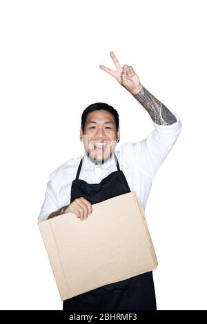 Cameriere degli uomini asiatici barbuto, chef vestito in grembiule nero è in possesso di cartone e mostra il segno di vittoria in bianco background.The concetto di protesta, attente Foto Stock