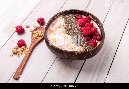 lamponi e semi di chia im ciotole di frullato con bacche congelate e granola.sana alimentazione in cocco naturale. Foto Stock