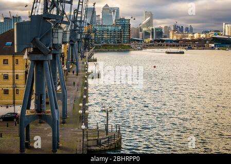 Londra, Inghilterra. Britannia Village e le sue gru viste dal Royal Victoria Dock Bridge con i grattacieli di Canary Wharf sullo sfondo. Foto Stock