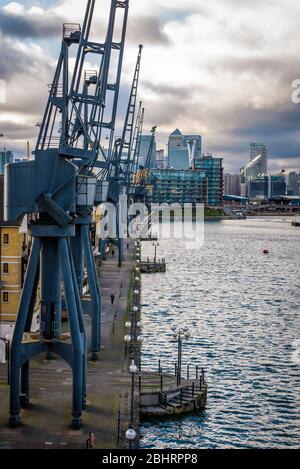 Londra, Inghilterra. Britannia Village e le sue gru viste dal Royal Victoria Dock Bridge con i grattacieli di Canary Wharf sullo sfondo. Foto Stock