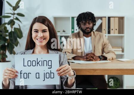 Dipendente che mostra cartellino con alla ricerca di un lavoro e di un reclutatore afro-americano in carica Foto Stock
