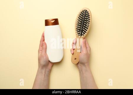 Le mani femminili tengono il flacone di shampoo e lo spazzolino su sfondo beige Foto Stock