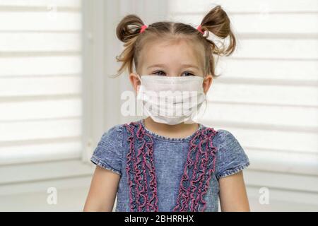 bambina in una maschera monouso che mostra stop gesture con palmo guardando dritto la fotocamera. Covid 19, il concetto di coronavirus.levandosi in piedi e sorridendo Foto Stock