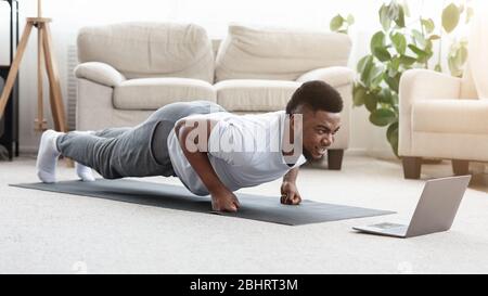 Esercizio sportivo Black Man Making Fist Plank davanti al notebook Foto Stock