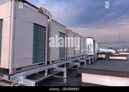 Unità di aria condizionata VRV HVAC, grande ventilatore e un radiatore dell'acqua su un tetto di nuovo edificio industriale con cielo blu e nuvole sullo sfondo. Foto Stock