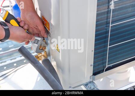 Il tecnico HVAC sta lavorando sulle unità del condizionatore d'aria su un tetto di un nuovo edificio industriale. Il tecnico utilizza una chiave fissa per serrare l'unità esterna di Foto Stock