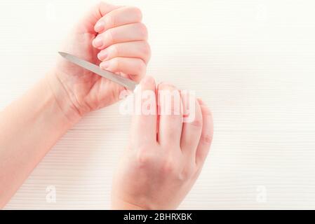 Mano della donna bianca con le unghie naturali sane ottenere procedura di cura della chiodo. Mani bianche femmina lacci lima unghie, isolati su bianco Foto Stock