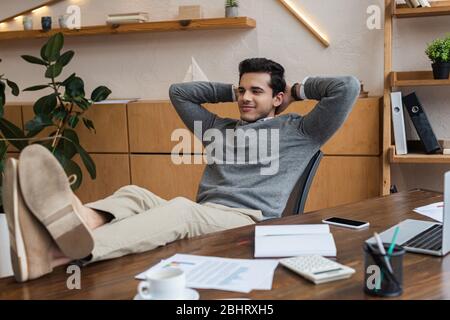 Uomo d'affari con le mani dietro la testa mettere le gambe sul tavolo in ufficio Foto Stock