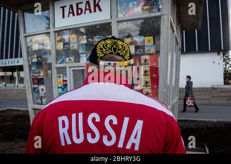 Mosca, Russia. 25 aprile 2015. Un uomo in abiti con simboli russi moderni guarda la finestra di un chiosco di tabacco con pacchetti di sigarette sovietiche sul vicolo principale del VDNH (Mostra dei risultati dell'economia nazionale) a Mosca, Russia Foto Stock