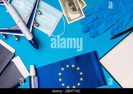 Vista dall'alto dell'aereo giocattolo, maschera medica con igienizzatore per le mani e bandiera dell'Unione europea su sfondo blu Foto Stock