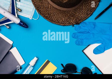 Vista dall'alto dell'aereo giocattolo vicino alla maschera medica, cappello con passaporti e guanto in lattice su sfondo blu Foto Stock