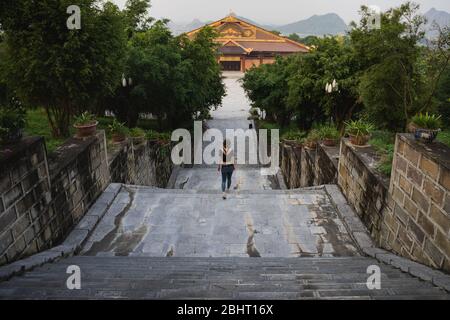 Giovane donna che scende le scale tra gli alberi nel tempio di Bai Dinh Foto Stock