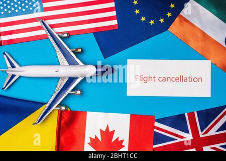 Vista dall'alto dell'aereo giocattolo vicino alla carta con scritta di cancellazione del volo e bandiere di paesi su superficie blu Foto Stock