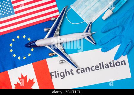 Vista dall'alto dell'aereo giocattolo, carta con scritta di cancellazione del volo vicino alla maschera medica e bandiere di paesi su superficie blu Foto Stock