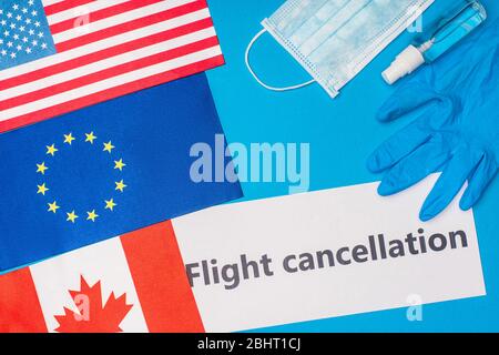 Vista dall'alto della carta con scritta di cancellazione del volo vicino alla maschera medica e bandiere di paesi su superficie blu Foto Stock