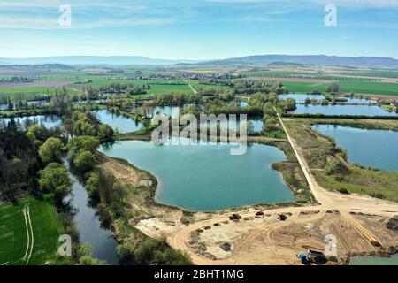 Veduta aerea di un attivo stagno ghiaia accanto al fiume Leine vicino Sarstedt, Germania, con un camion e mucchi di sabbia e un villaggio sullo sfondo Foto Stock