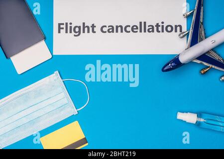 Vista dall'alto della carta con scritta di cancellazione del volo, maschera medica, carta di credito e aereo giocattolo su sfondo blu Foto Stock