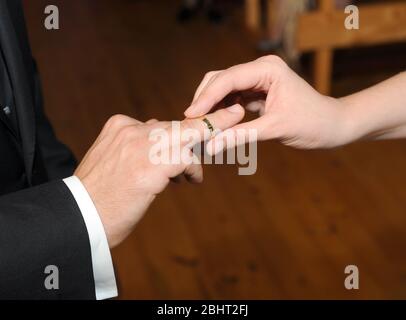 Vista di un anello d'oro che una donna sta mettendo sul suo futuro marito durante il loro matrimonio. Foto Stock