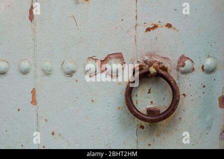 Cancello in legno verde chiaro con un batticalcagno in ferro arrugginito a forma di cerchio. Via di Essaouira, Marocco. Foto Stock