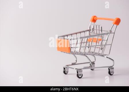 Concetto di shopping. Foto ravvicinata del piccolo carrello a spinta con elementi arancioni isolati su sfondo grigio con spazio vuoto per la copia Foto Stock