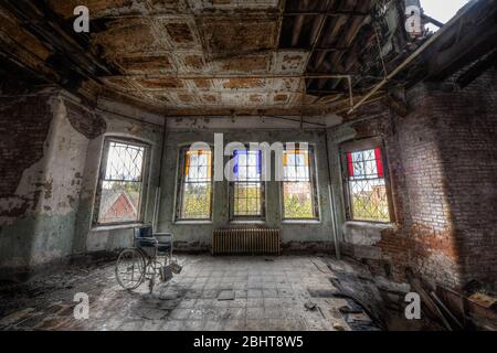 Sedia a rotelle di fronte alle vetrate colorate nell'area comune di uno storico Ospedale abbandonato Foto Stock