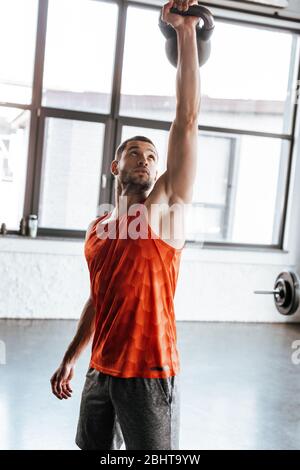 sportivo forte che tiene pesante manubri sopra la testa mentre si esercita in palestra Foto Stock