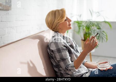 profilo di donna matura che fuma in unione con marijuana legale e posacenere in possesso Foto Stock