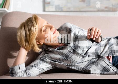 donna felice e matura che giace sul divano e tiene unito con marijuana legale Foto Stock