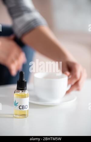 fuoco selettivo della bottiglia con la scritta cbd vicino donna matura che tocca la tazza di tè Foto Stock
