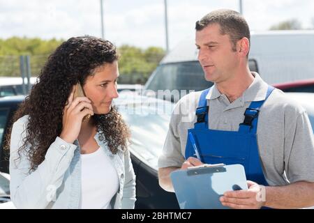 donna cliente che chiama marito in officina di riparazione auto Foto Stock