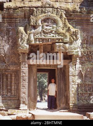 Giovane ragazzo in piedi in antico portale, Ta Prohm Tempio, Siem Reap, Regno di Cambogia Foto Stock