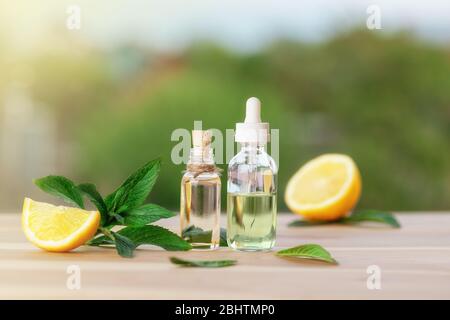 Bottiglie con olio di menta, limone e foglie di menta verde fresca su tavola di legno. Sfondo sfocato. Foto Stock