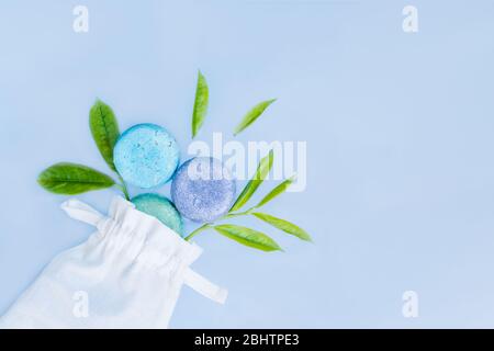 Vista dall'alto tre pezzi rotondi di sapone naturale fatto a mano con foglie fresche verdi che volano fuori dalla borsa in tessuto bianco su sfondo azzurro. Corpo naturale ca Foto Stock