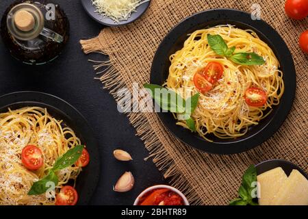 Due piatti neri con verdure vegetariane, gustosi spaghetti classici italiani con basilico, salsa di pomodoro, parmigiano e olio d'oliva al burlap su un Foto Stock