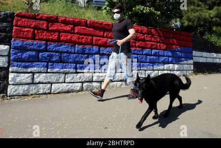 Belgrado, Serbia. 27 aprile 2020. Un uomo che indossa una maschera protettiva passa accanto alla bandiera serba con il suo cane durante una giornata calda e soleggiata, in mezzo alla pandemia coronavirus COVID-19 in corso. I cittadini serbi stanno lentamente tornando alla vita normale, poiché le autorità hanno facilitato alcune delle misure adottate per limitare la diffusione del coronavirus SARS-cov-2 che causa la malattia COVID-19. Credit: Koca Sulejmanovic/Alamy Live News Foto Stock