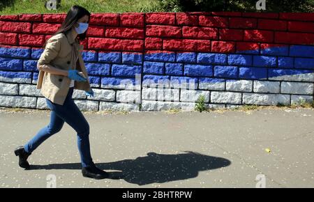 Belgrado, Serbia. 27 aprile 2020. Una donna che indossa una maschera protettiva e guanti passa accanto alla bandiera serba durante una giornata calda e soleggiata, in mezzo alla pandemia coronavirus COVID-19 in corso. I cittadini serbi stanno lentamente tornando alla vita normale, poiché le autorità hanno facilitato alcune delle misure adottate per limitare la diffusione del coronavirus SARS-cov-2 che causa la malattia COVID-19. Credit: Koca Sulejmanovic/Alamy Live News Foto Stock