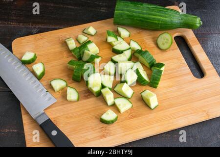 Tritare un cetriolo senza spighe: Tagliare un cetriolo inglese in pezzi su un tagliere di bambù Foto Stock