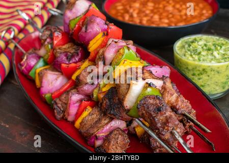 Spiedini di bistecca Fajita con Cilantro Chimichurri: Kabob di manzo e verdure alla griglia serviti con salsa di chimichurri e fagioli pinto Foto Stock