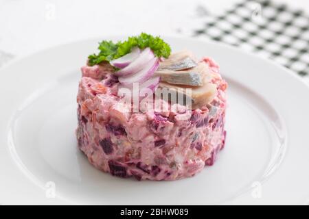 Insalata russa di aringhe sotto un cappotto di pelliccia. Su un piatto bianco, primo piano. Foto Stock