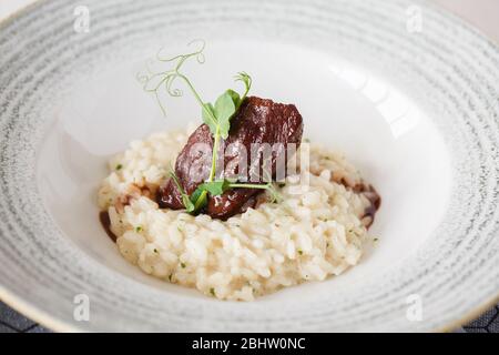 Risotto di manzo servito in un piatto con salsa e decorazione micro-verde. Primo piano. Foto Stock