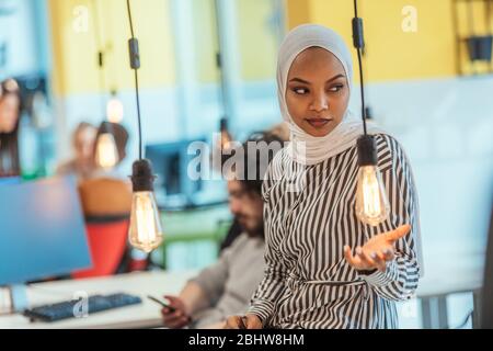 Protarit di una donna musulmana nera (afro-americana) in piedi in un moderno ufficio d'affari mentre indossa un hijab. Foto Stock