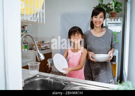 Aiuto mano. Cute Little Girl aiuta la sua madre nel lavare i piatti alla cucina familiare Foto Stock
