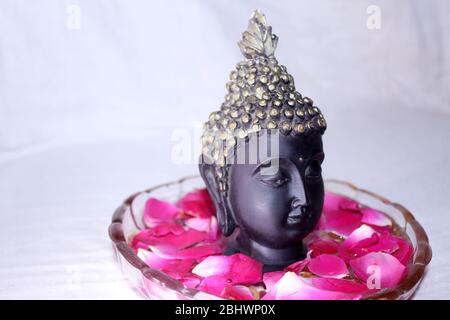 buddha dio faccia tra petali di rosa in ciotola, sfondo spa Foto Stock